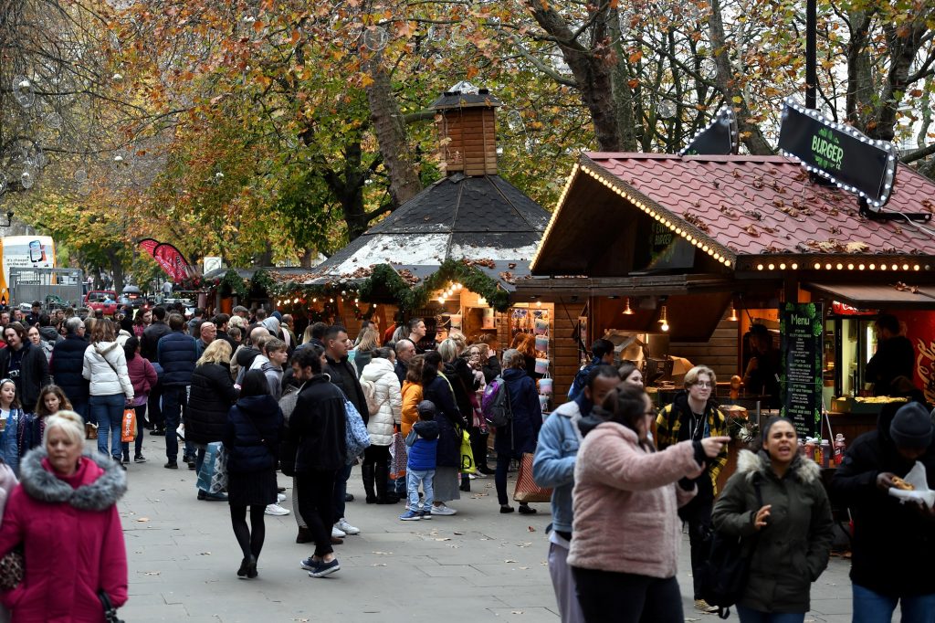 Christmas market on pedestrian area.  Wooden chalets with medium gathering of people looking at a stall.